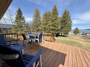 A wooden deck with outdoor furniture, overlooking a grassy area with trees and a body of water.