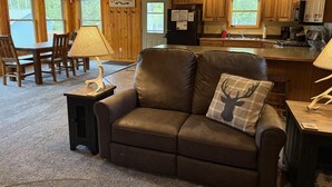 L’intérieur chaleureux d’un chalet comprend un coin repas, un canapé en cuir et une cuisine avec des meubles en bois.