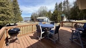 Une terrasse en bois avec une table et des chaises, un barbecue et une vue sur un lac et des bâtiments.