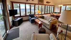 A cozy living room with a large window overlooking a rocky landscape, a television, and a dining area with a table and chairs.
