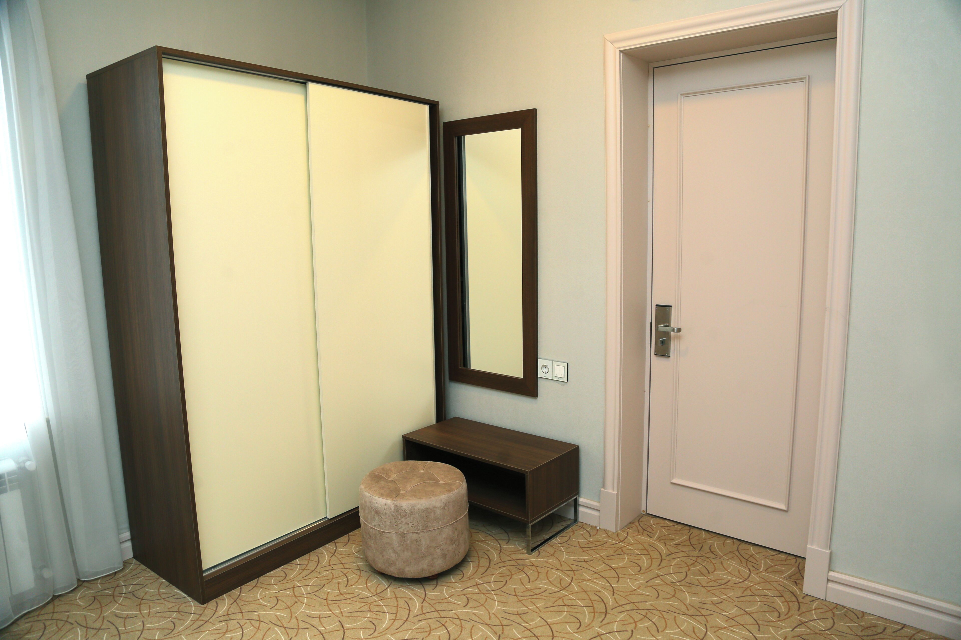 A room with a wardrobe, a mirror, a bench, and a door.