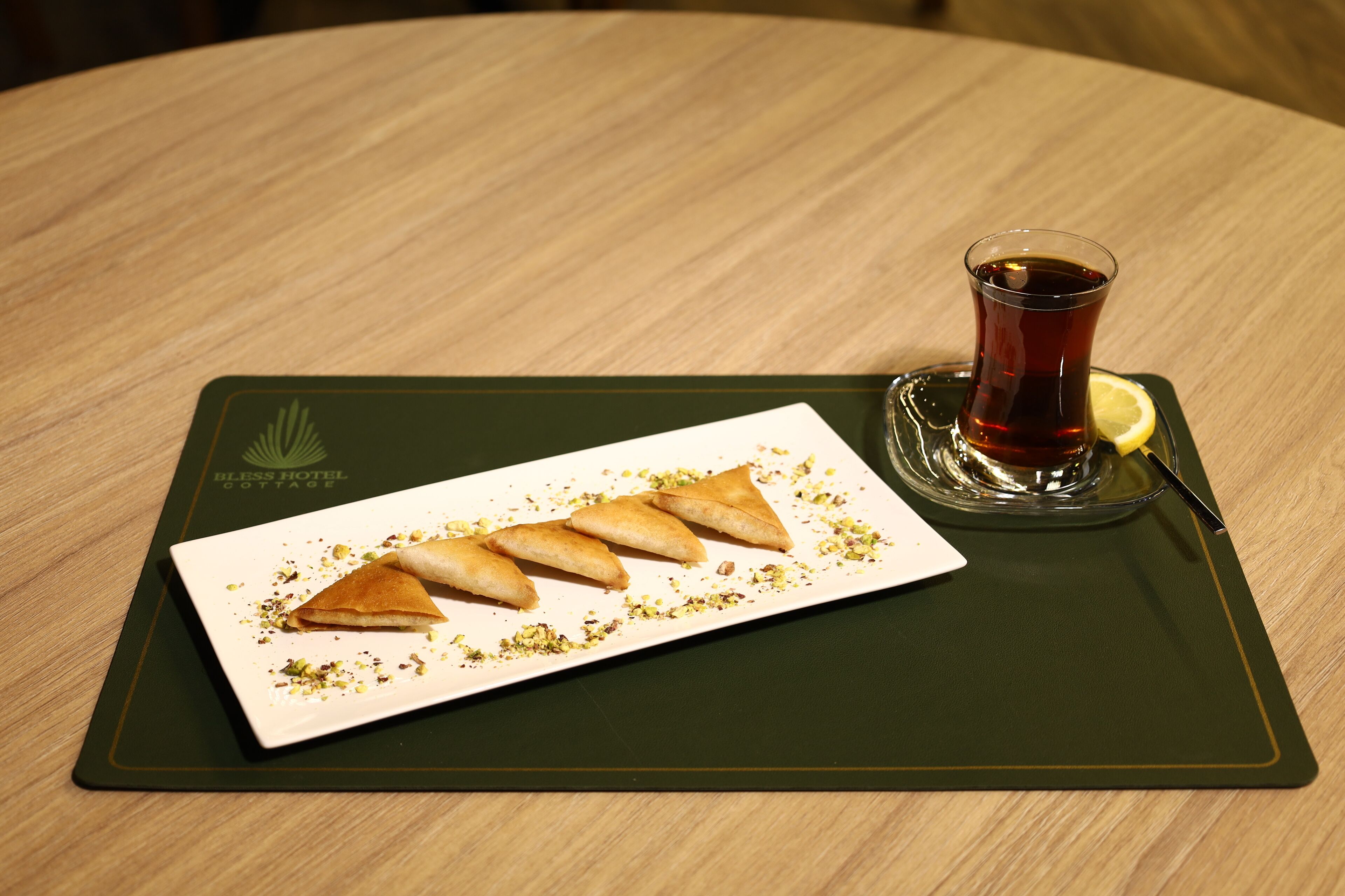 A plate of triangular pastries with a glass of tea on a wooden table.