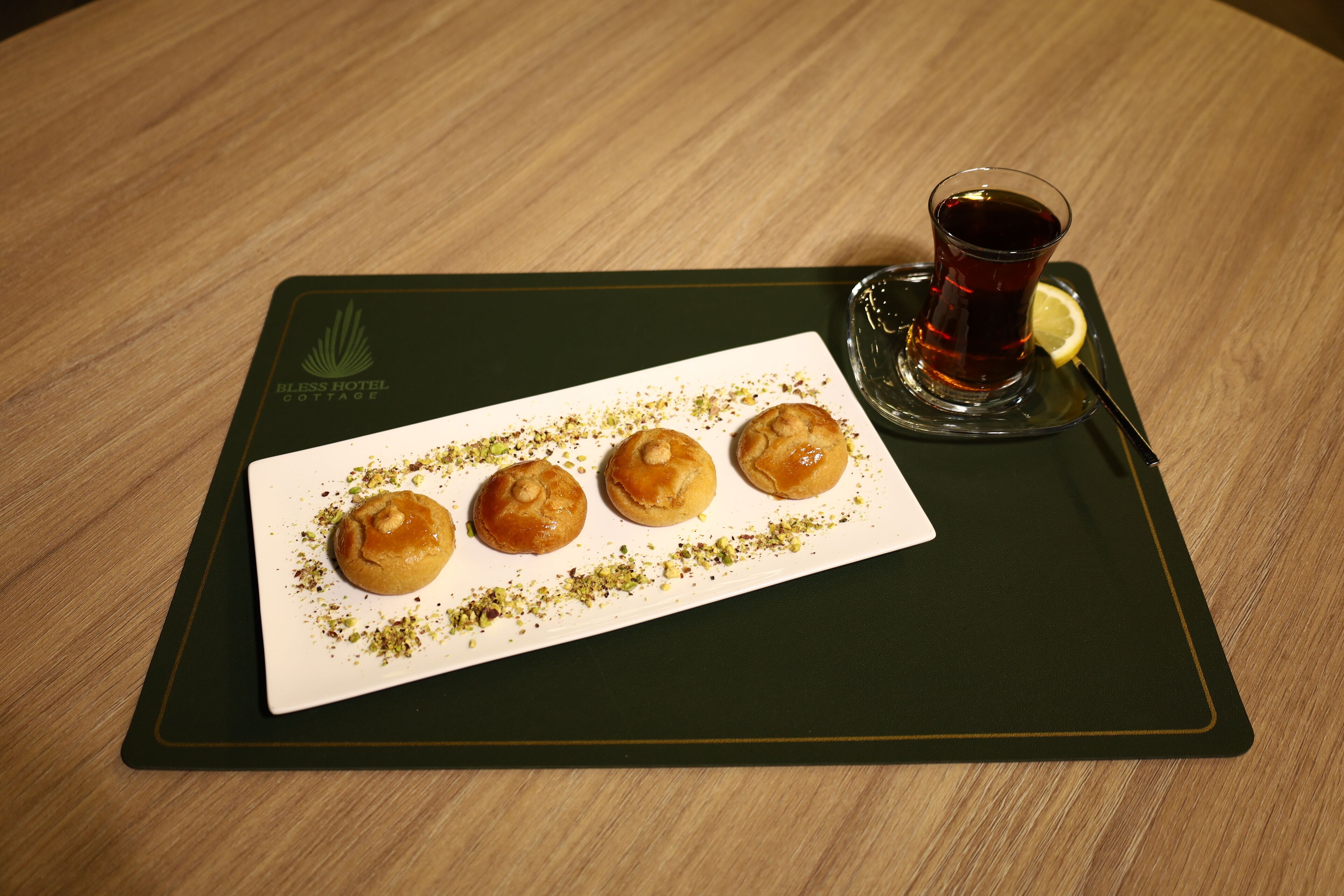 Een dienblad met vier gebakjes en een glas thee op een houten tafel.