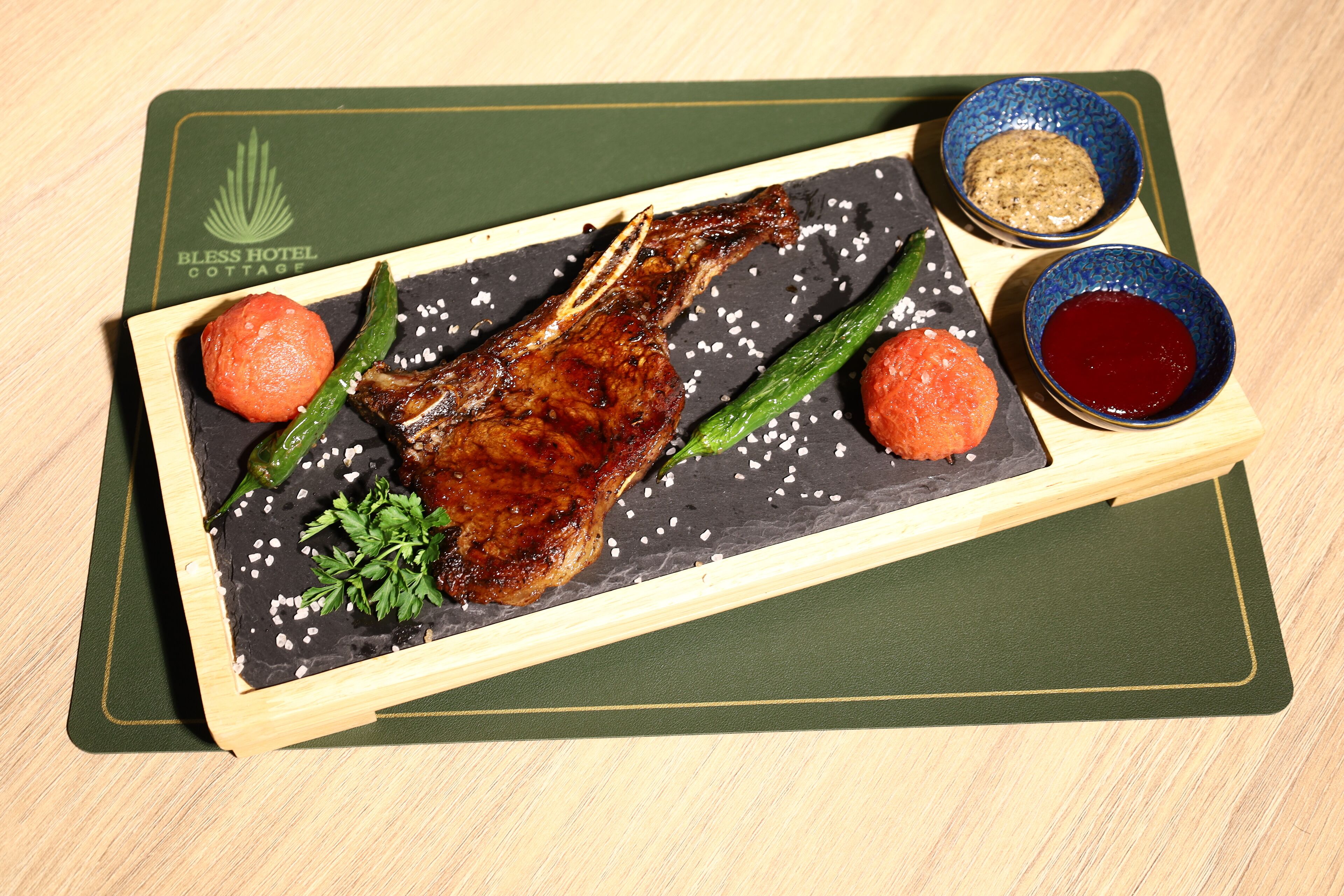 Una tabla de madera con cordero asado, judías verdes y dos salsas redondas sobre un plato de pizarra.