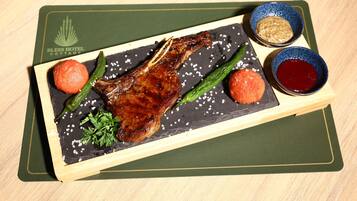 Una tabla de madera con cordero asado, judías verdes y dos salsas redondas sobre un plato de pizarra.