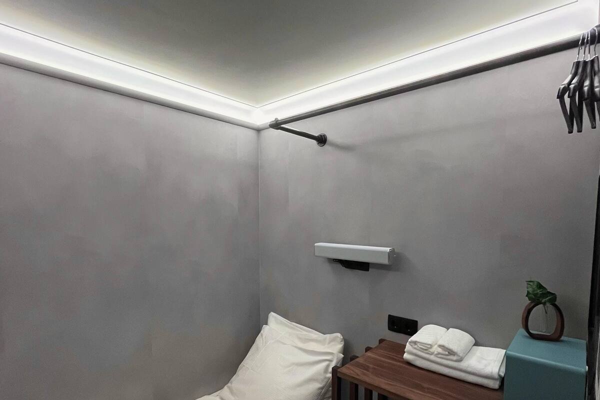 A small, modern bedroom with a single bed, a small table with a plant, and a wall-mounted shelf.