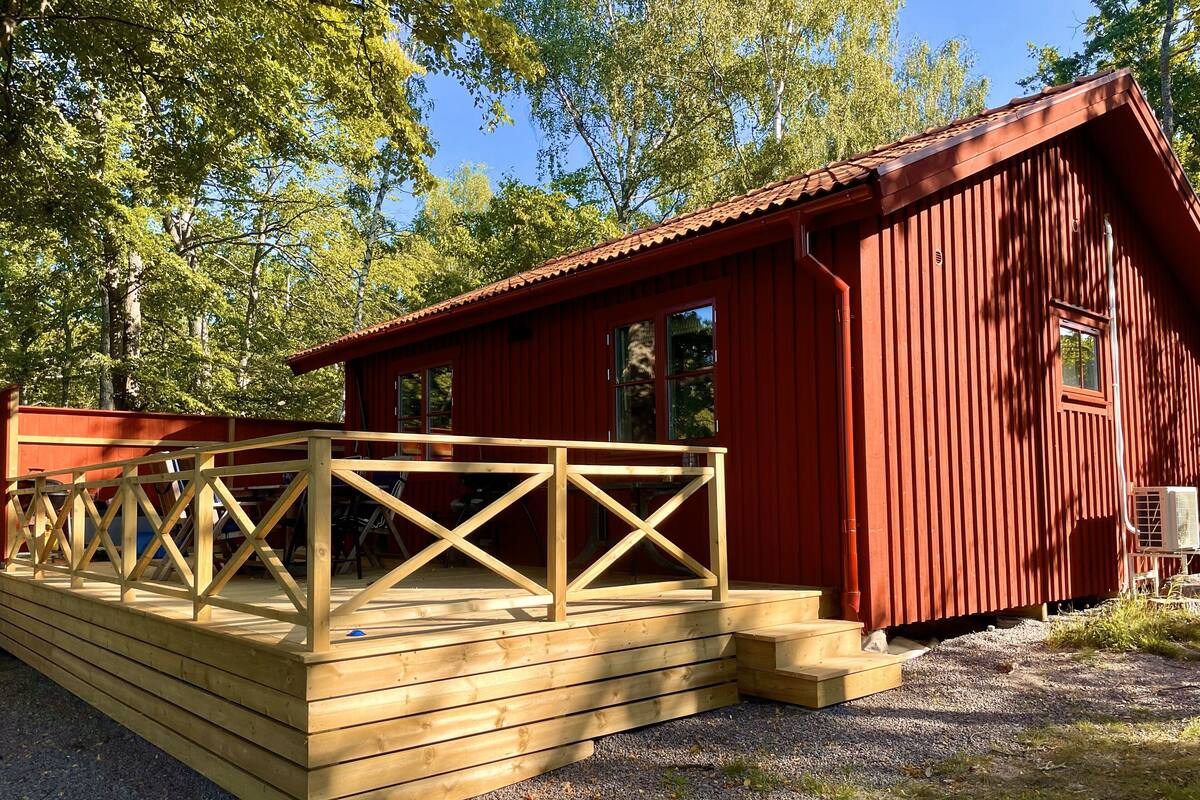 A red wooden cabin with a wooden deck and a small porch.
