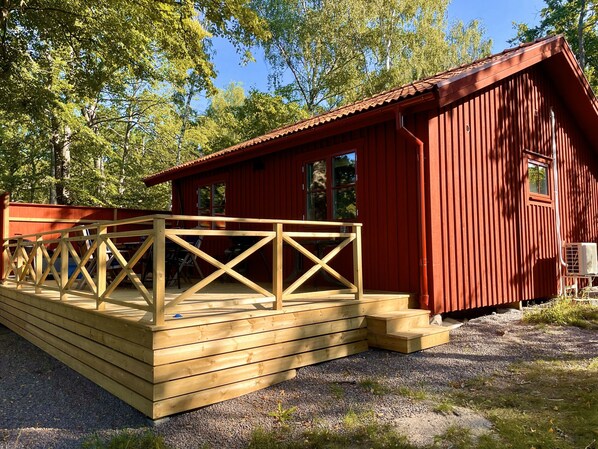 Una cabaña roja de madera con un porche pequeño y una terraza de madera.