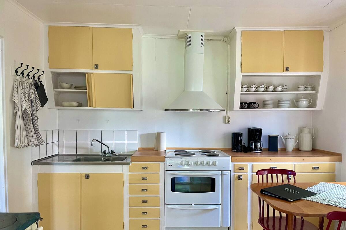 A compact kitchen with a stove, oven, and sink, featuring yellow cabinets and a wooden countertop.