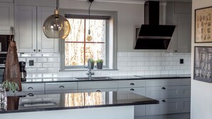 Una cocina moderna con armarios blancos, encimera negra, un amplio ventanal con vistas y una lámpara colgante.