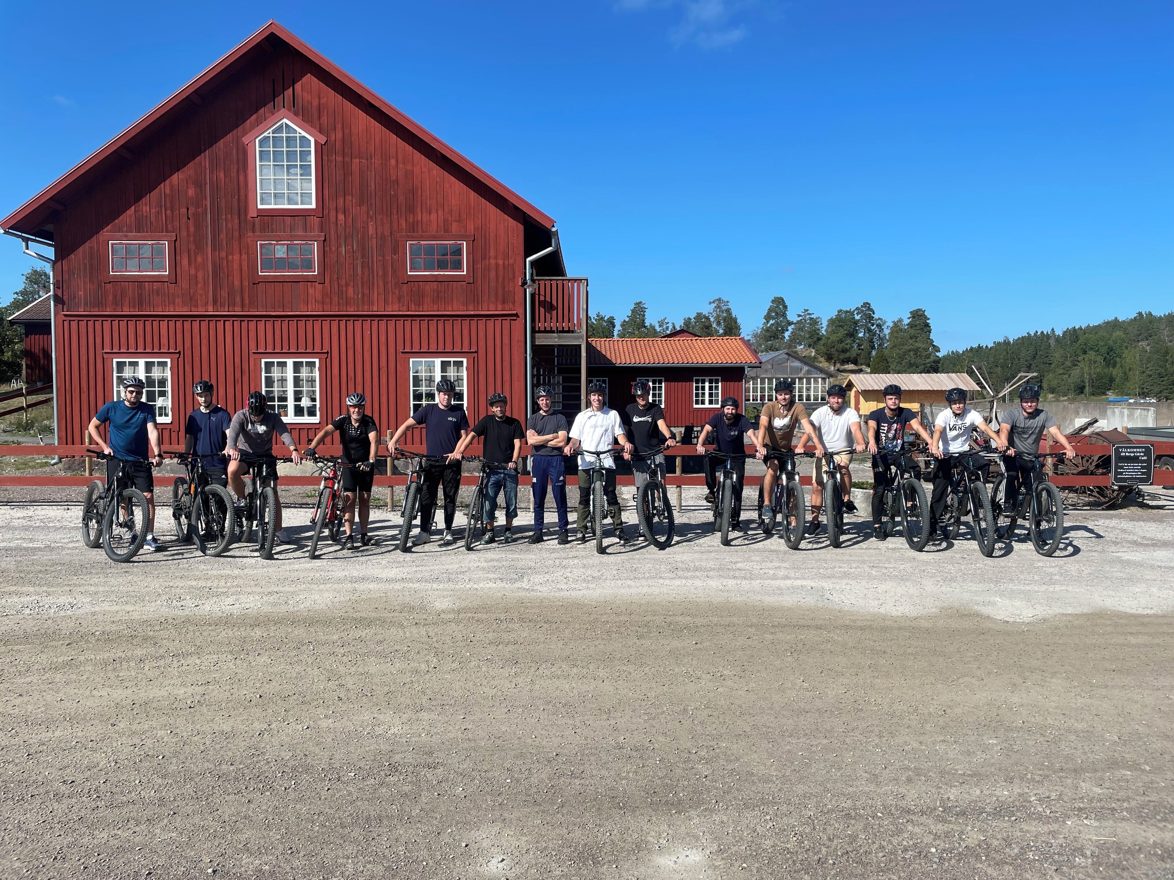 A group of people on bicycles in front of a red barn.