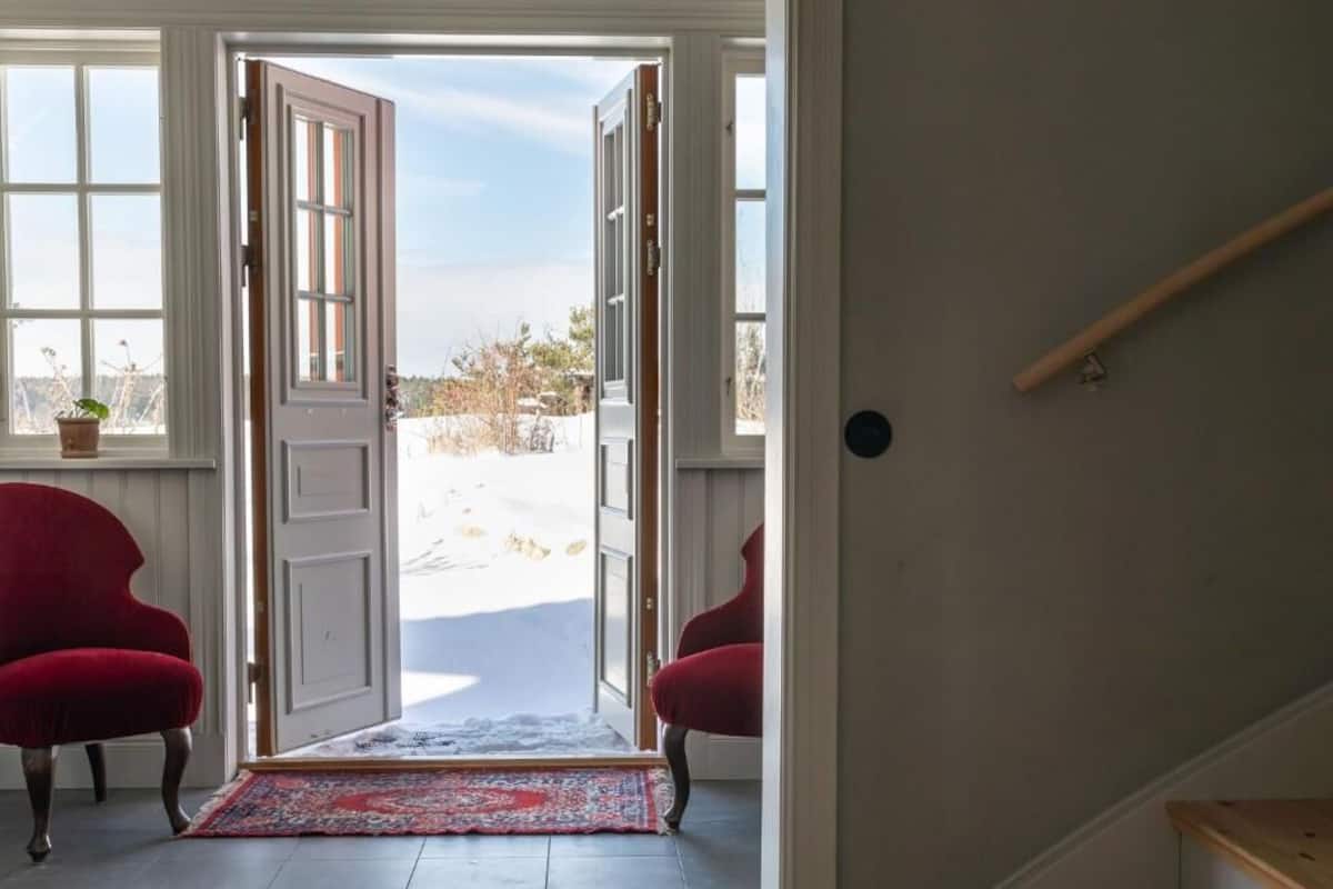 A room with a large open door leading outside, a red chair, and a small table with a plant.
