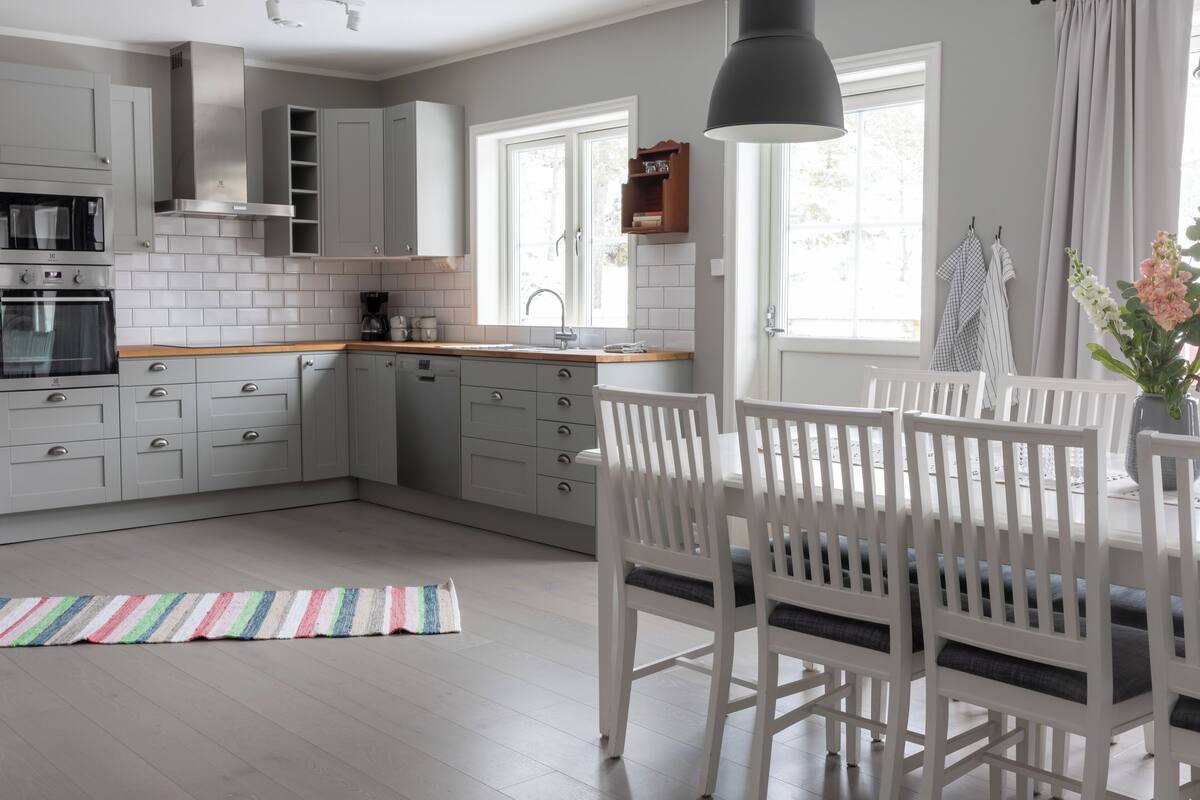 A modern kitchen with white cabinets, a wooden countertop, and a dining area with white chairs and a table.