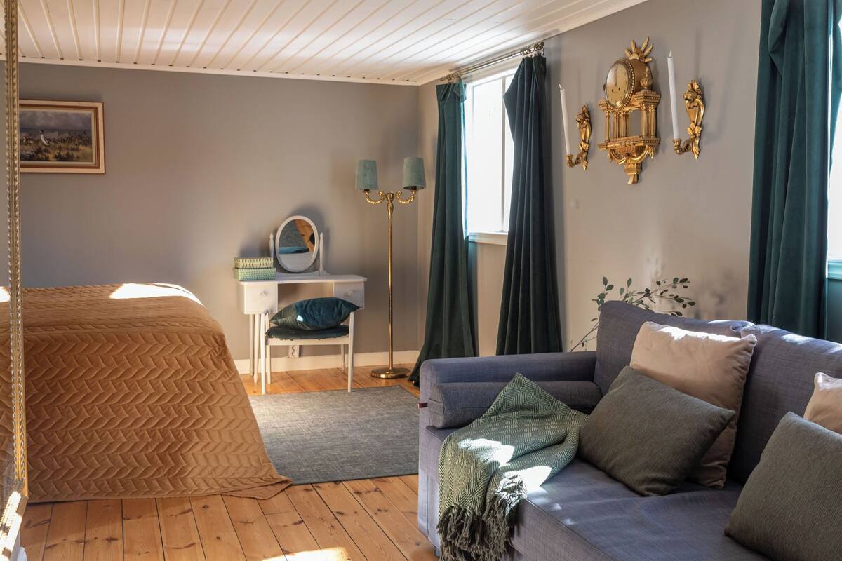 A room with a bed, a sofa, a desk, a mirror, and a wall clock.