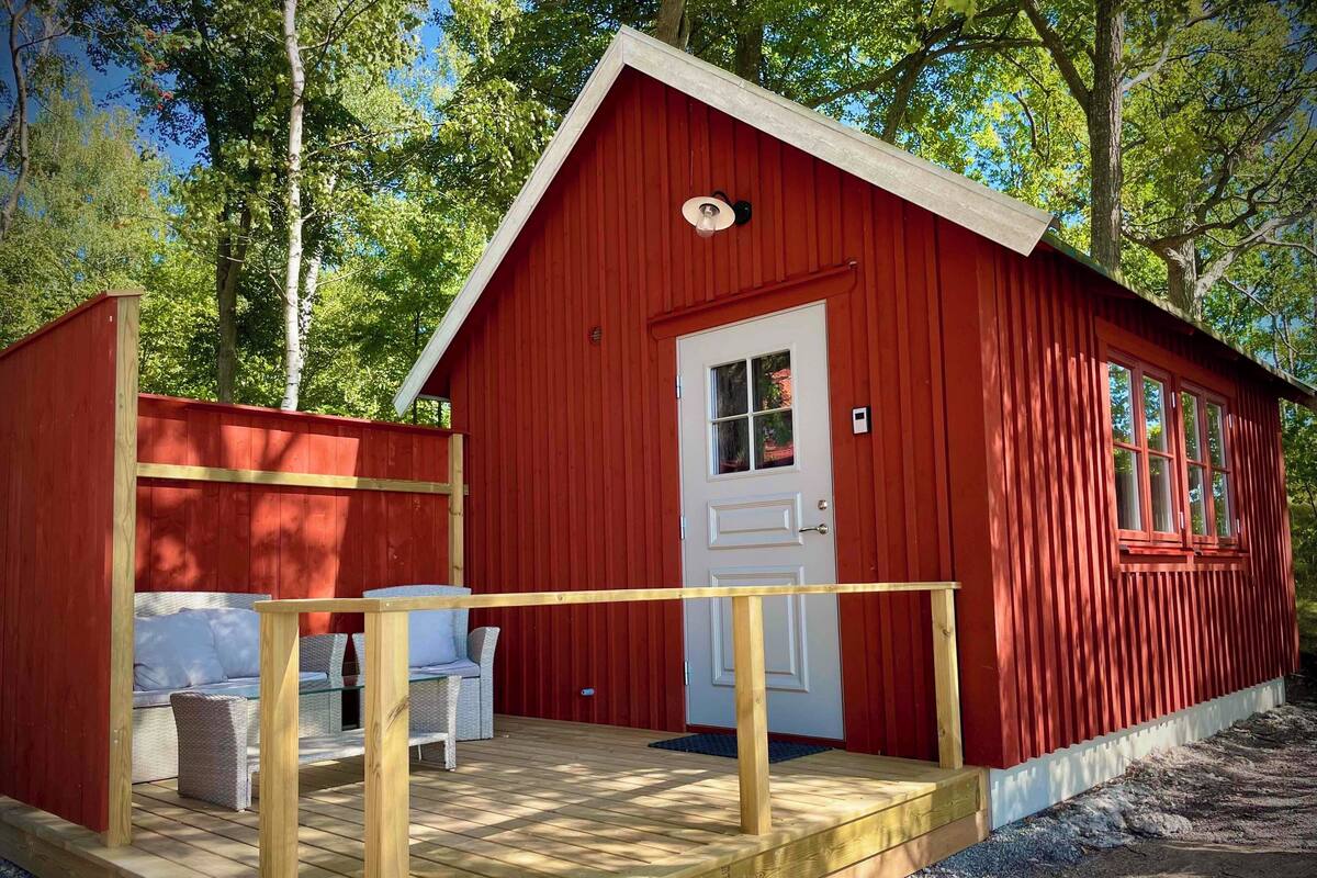 A red wooden cabin with a white door, a small porch with a bench, and a window.
