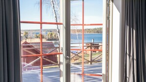 Una habitación con un amplio ventanal corredero que da a una terraza exterior con vista a un lago y un granero rojo.