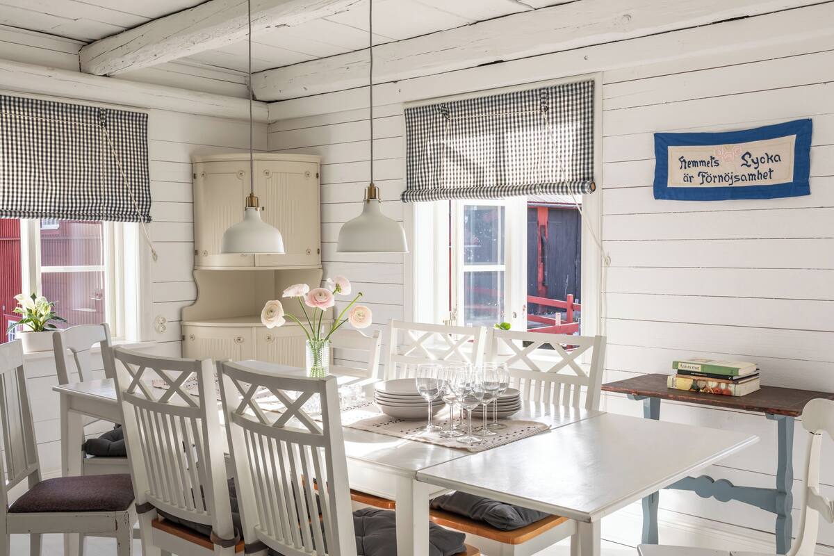 A dining area with white wooden furniture, checkered window valances, and a sign on the wall.