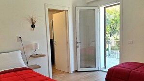 A hotel room with two beds, a small bedside table with a lamp, a wall-mounted decorative item, and a sliding glass door leading to an outdoor area. - Granatelli Holiday Home (Altavilla Milicia)