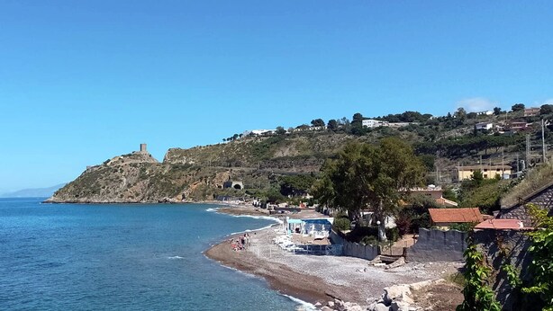 A coastal view with a beach, rocky hillside, and a lighthouse. - Granatelli Holiday Home (Altavilla Milicia)