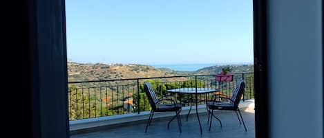 Un balcón con mesa y sillas, que ofrece vistas a un paisaje montañoso y al mar.