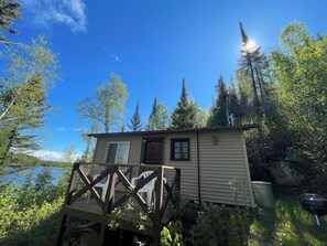 A small cabin with a deck, surrounded by trees and a body of water. - Cabin 5 "Dockside" 1 BR, 2 pp, lakefront, access to boats! (ely)