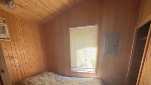 Eine kleine, einräumige Holzhütte mit Bett und Fenster.