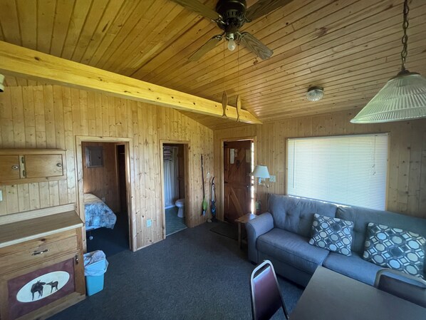 A wooden cabin interior with a sofa, a wooden cabinet, and a ceiling fan. - Cabin 5 "Dockside" 1 BR, 2 pp, lakefront, access to boats! (ely)