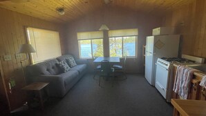 Ein gemütliches Blockhäuschen-Interieur mit einer Couch, einem Esstisch, Stühlen, einem Kühlschrank und einem Herd.