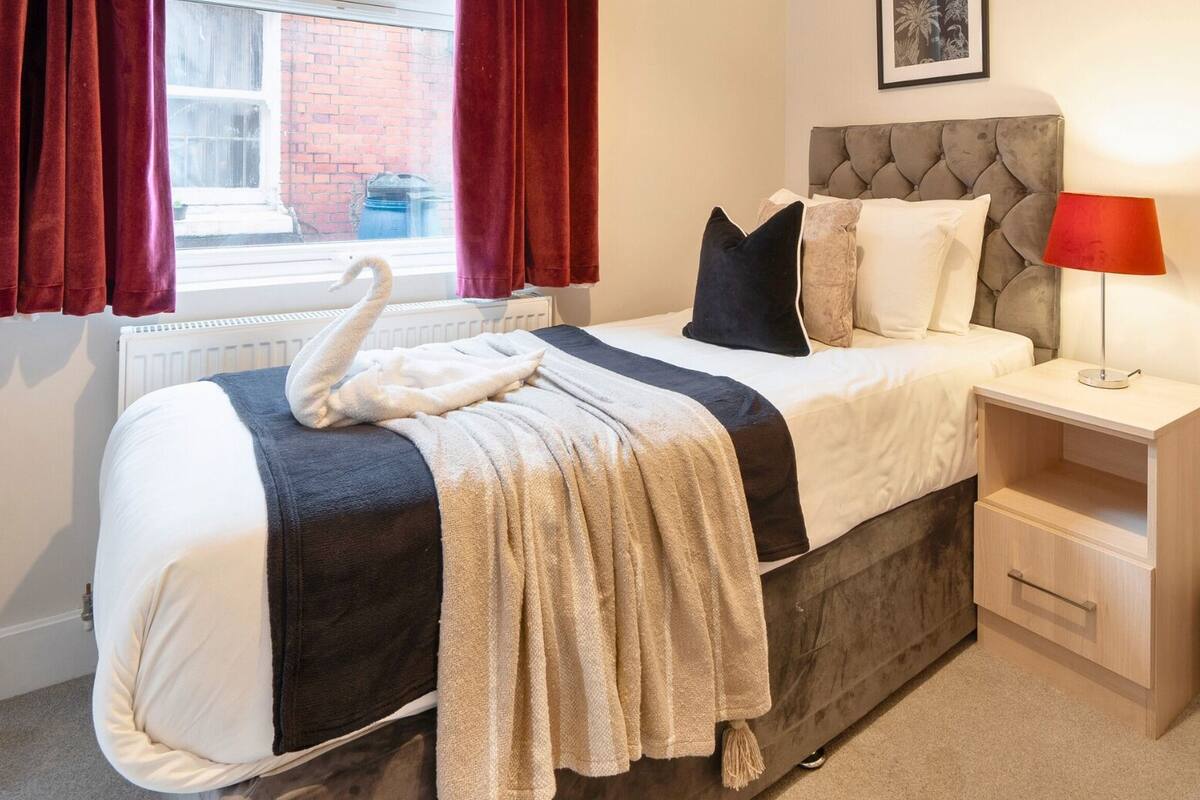 A neatly made bed with a swan-shaped pillow, a bedside lamp, and a small wooden nightstand.