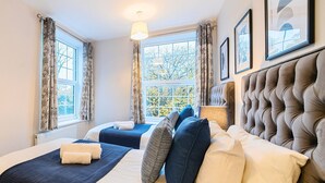 A hotel room with two beds, a large window with a view, and a tufted headboard. - Everest Lodge Serviced Apartment (Farnborough)