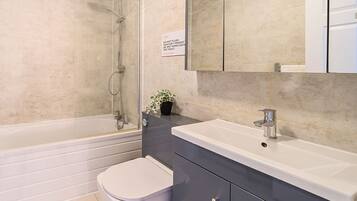 A modern bathroom with a glass-enclosed shower, a white toilet, a sink with a mirror, and a potted plant.