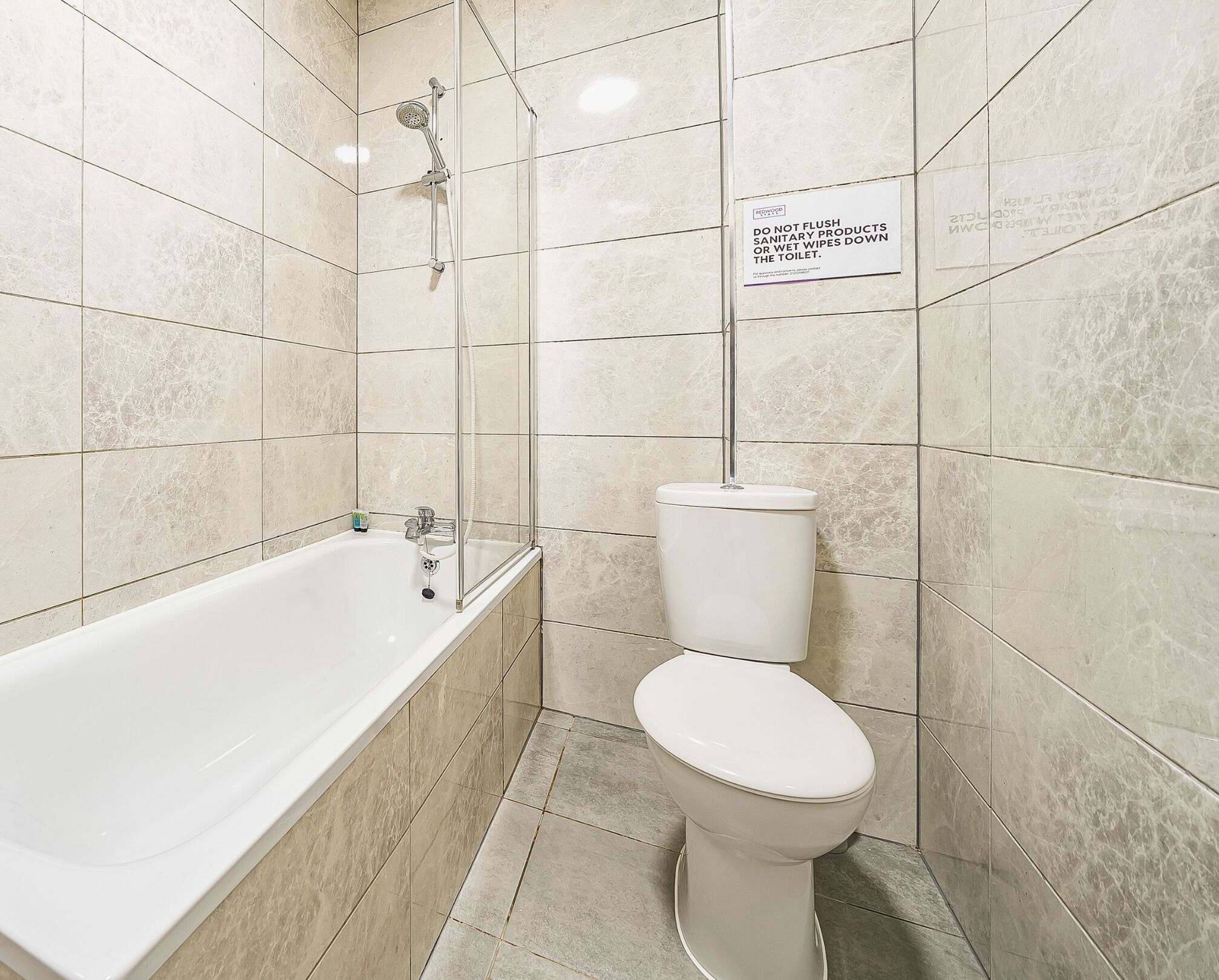 A bathroom with a bathtub, toilet, and a shower enclosure. A sign instructs not to flush sanitary products or wet wipes down the toilet.