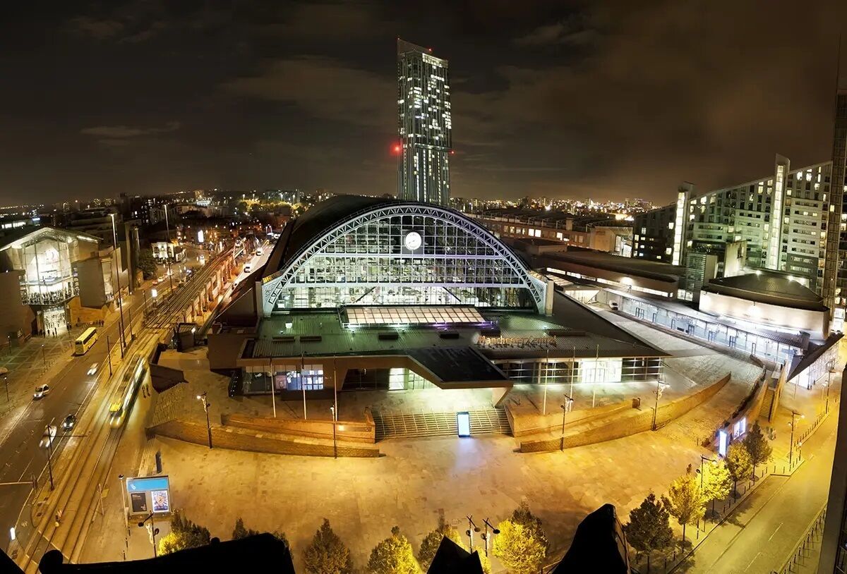 A modern building with a large glass facade and a curved roof, surrounded by a well-lit urban area with roads and other buildings.