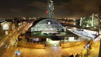 A modern building with a large glass facade and a curved roof, surrounded by a well-lit urban area with roads and other buildings.