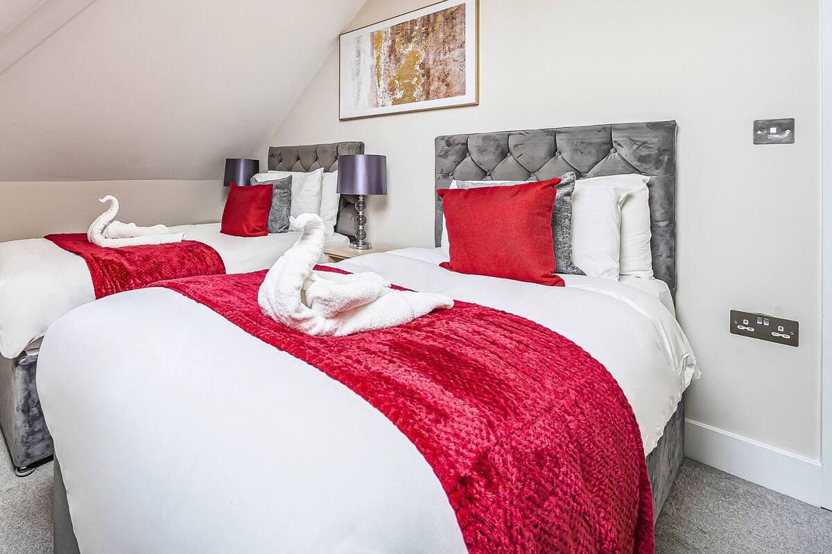 A hotel room with two beds, each with a red blanket and a white towel shaped like a swan.