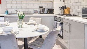 A modern kitchen with white cabinetry, a dining area with a round table set for four, and a small island with a sink. - Everest Lodge Serviced Apartment (Farnborough)