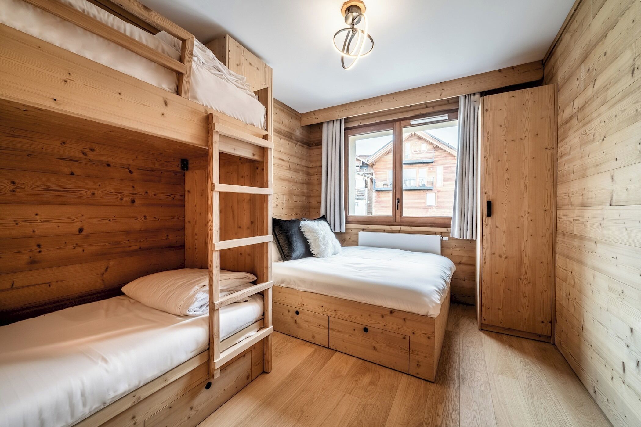A wooden cabin room with bunk beds, a ladder, a window with curtains, and a wooden door.