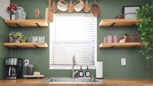 A kitchen with wooden shelves, a coffee maker, and a window with blinds. - Cottage 2 mi to Broadway: King Bed, Fenced Yard (Nashville)