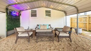 A covered patio area with a white wall, two windows, and a neon sign. - Cottage 2 mi to Broadway: King Bed, Fenced Yard (Nashville)