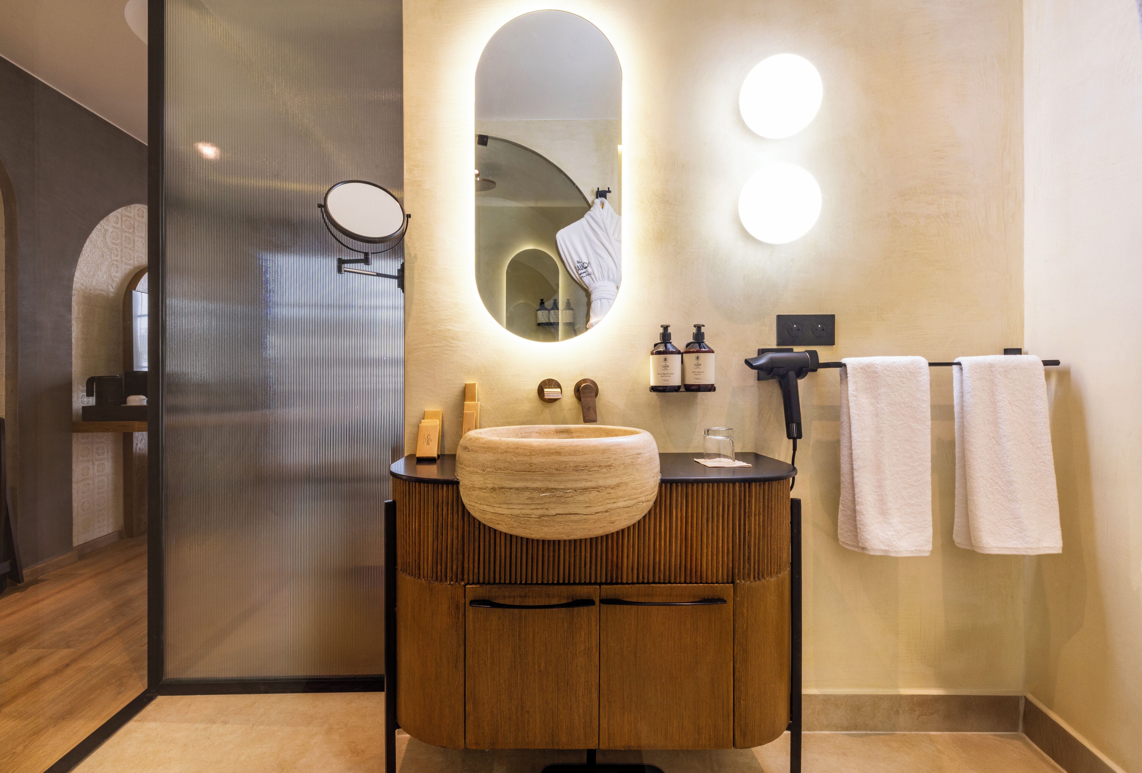 A modern bathroom with a wooden vanity, a large mirror, and two round lights on the wall.