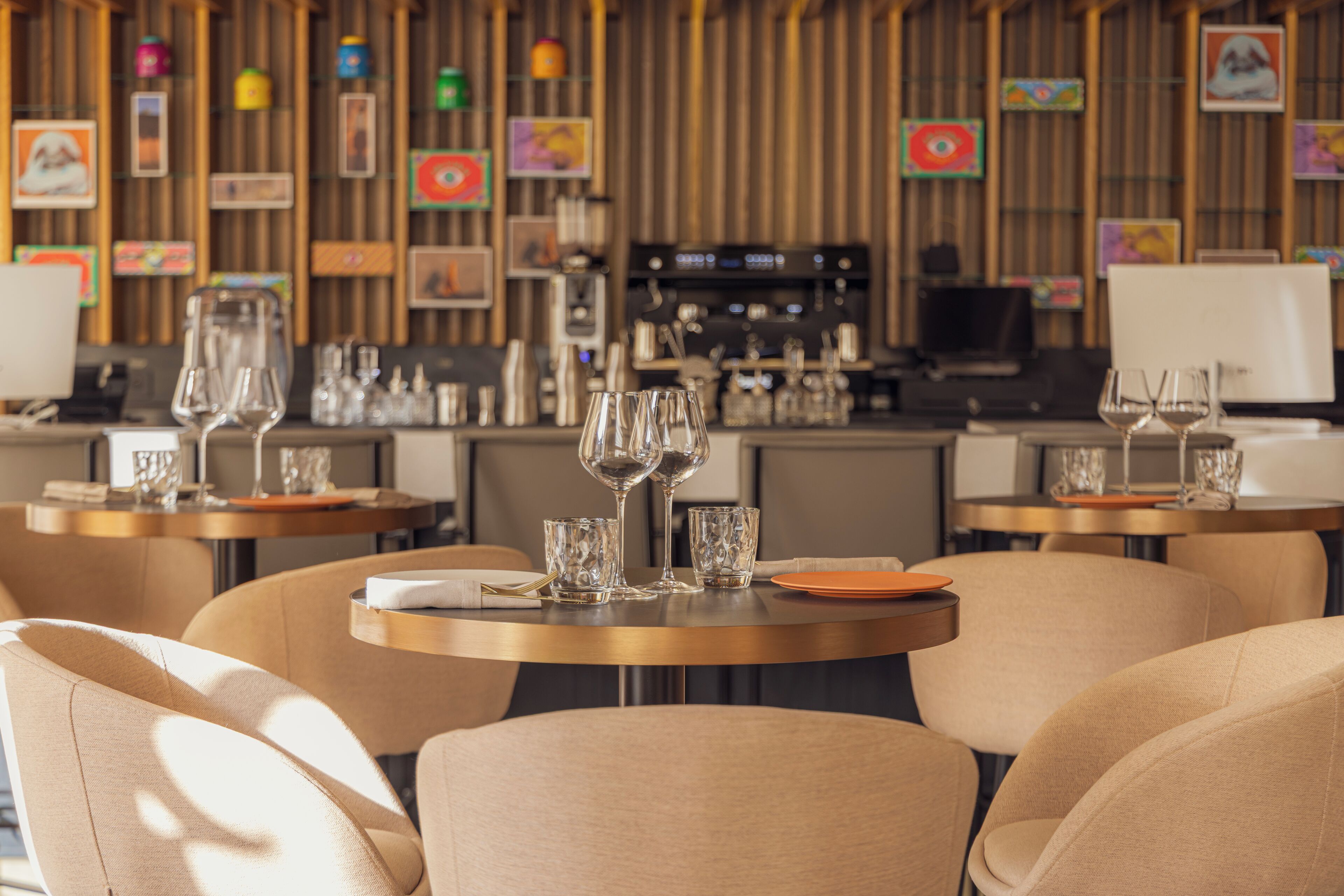 Un restaurant moderne avec des tables rondes, des chaises et un coin bar équipé d’une machine à café.