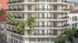 Un hotel de varios pisos con balcones, entrada a nivel de calle y palmeras.