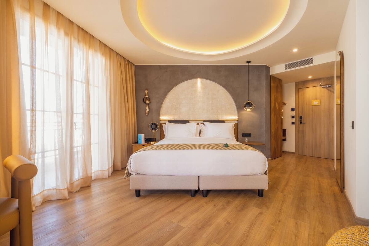 Une chambre moderne avec un grand lit, un luminaire au plafond au design incurvé et un plancher en bois.