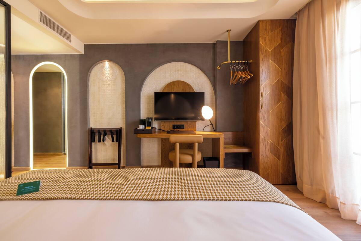 Une chambre d’hôtel moderne avec un grand lit, un bureau avec une télévision et un miroir.