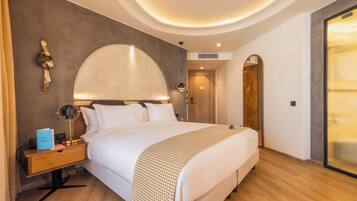Ein modernes Hotelzimmer mit einem großen Bett, einem Holfnachtkästchen, einer Schreibtischlampe und einem großen Spiegel.