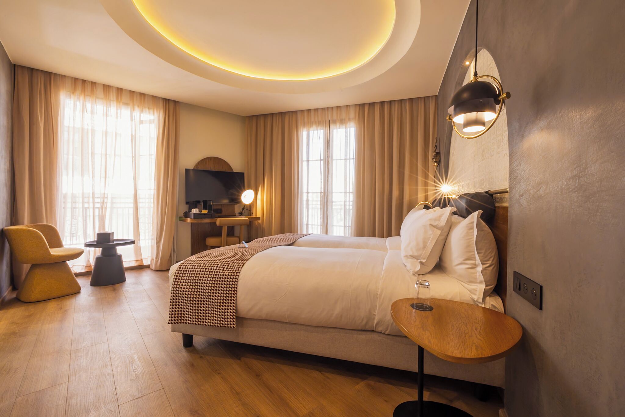 A modern hotel room with a large bed, a desk, a chair, and a round table.