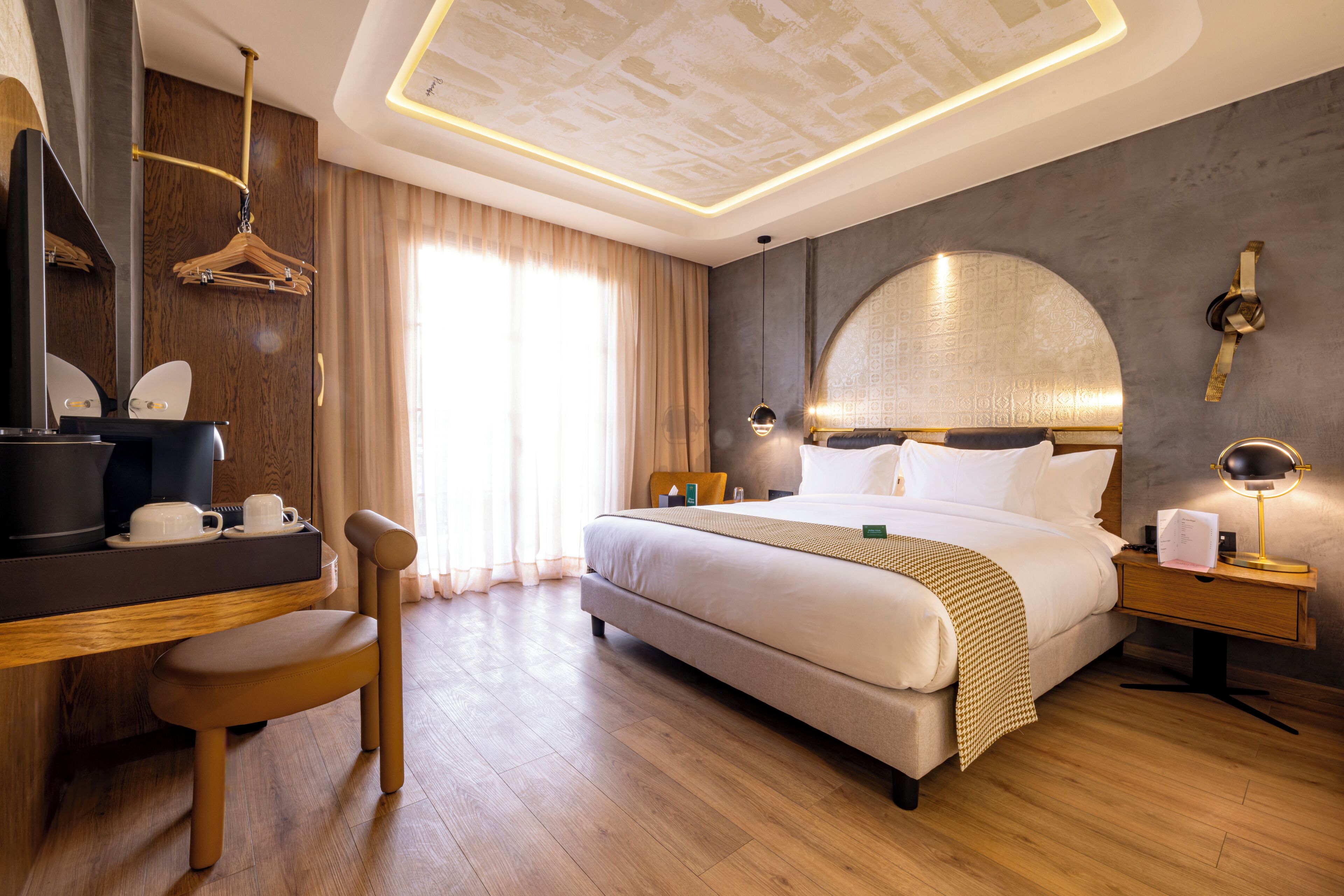 Ein Hotelzimmer mit einem großen Bett, einem Schreibtisch mit Stuhl, einem Kleiderschrank, einem Spiegel und einem Nachttisch mit Lampe.