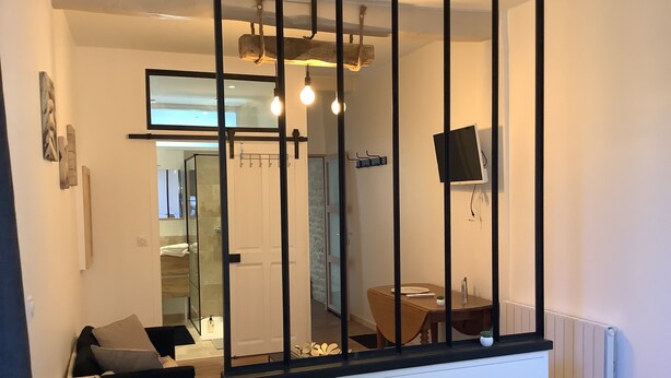 Een slaapkamer met een bed, een klein tafeltje met stoel, een aan de muur bevestigde televisie en een raam met gordijnen.