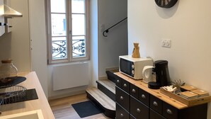 Een kleine keuken met een raam, een magnetron, een koffiezetapparaat en een houten kast.