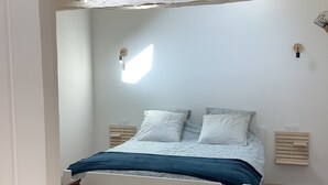 Een slaapkamer met een bed, houten hoofdbord, nachtkastjes en een bankje.